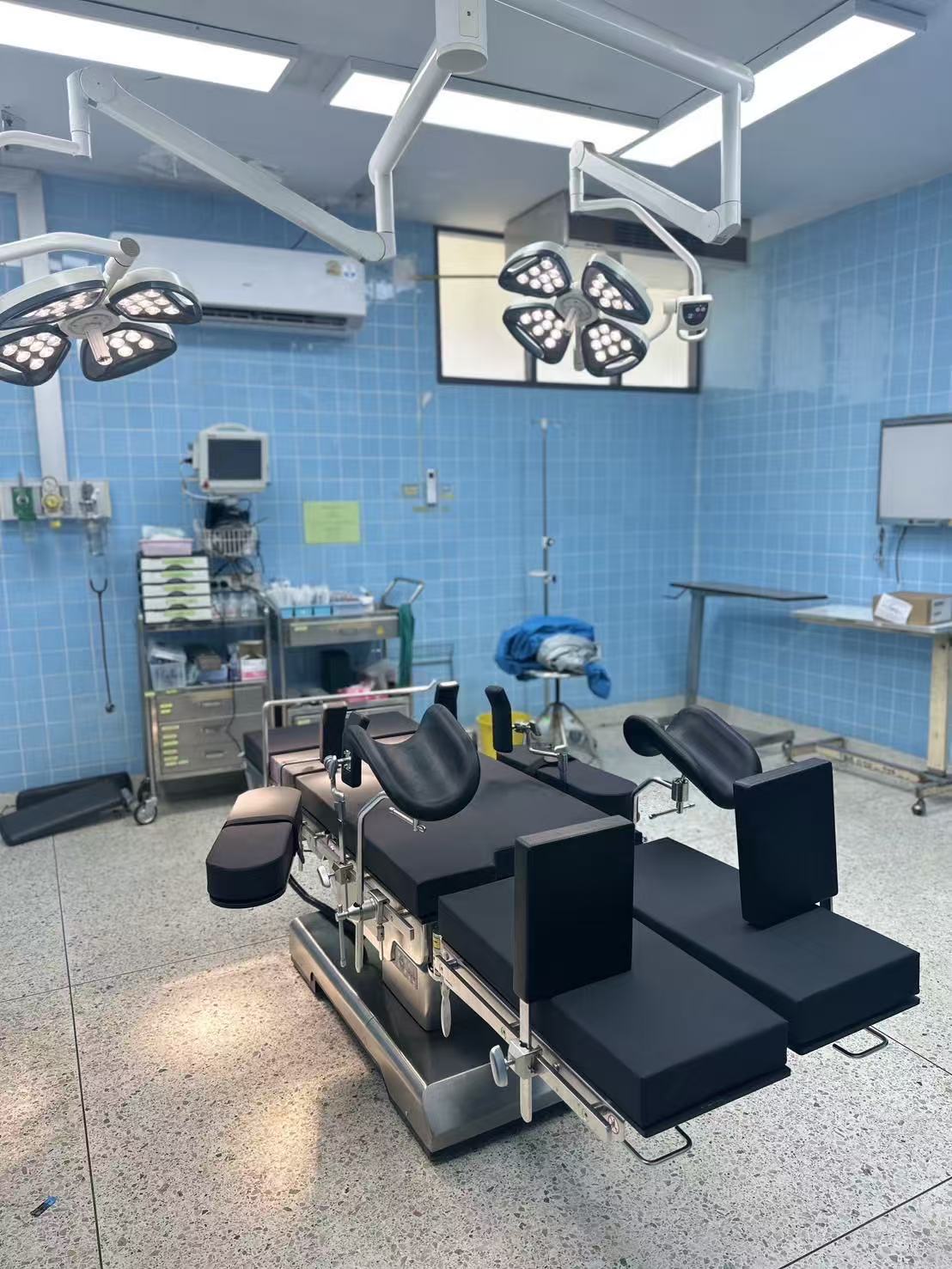 Wide-angle view of Saraphi Hospital operating room showing the TDY-Y-2 electro-hydraulic operating table with pendant surgical lights and stainless steel equipment trolleys