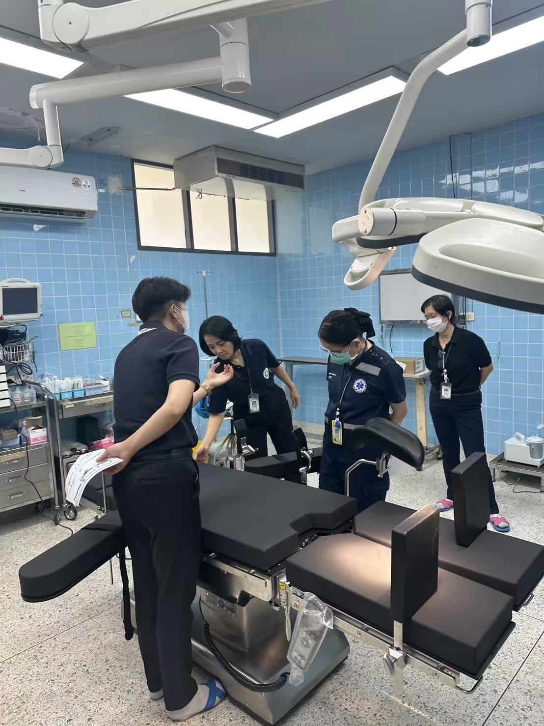 Saraphi Hospital operating-room staff inspecting the TDY-Y-2 electro-hydraulic multifunctional operating table during on-site clinical evaluation, with surgeons and nurses reviewing documentation